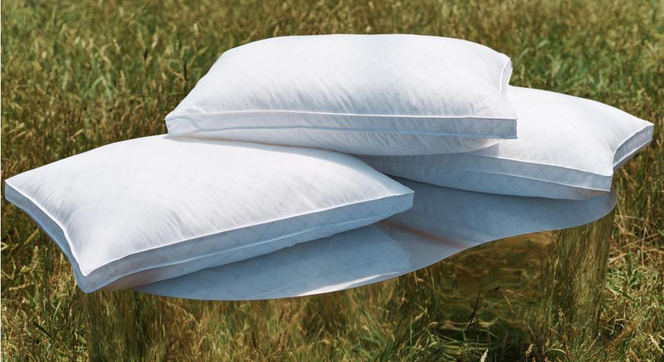 Photo of three pillows stack on top of one another. They're sitting on top of a mirrored podium in a grass field.