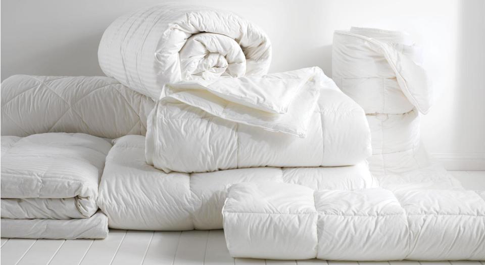 A stack of folded and rolled up quilts sitting on a white timber floor.