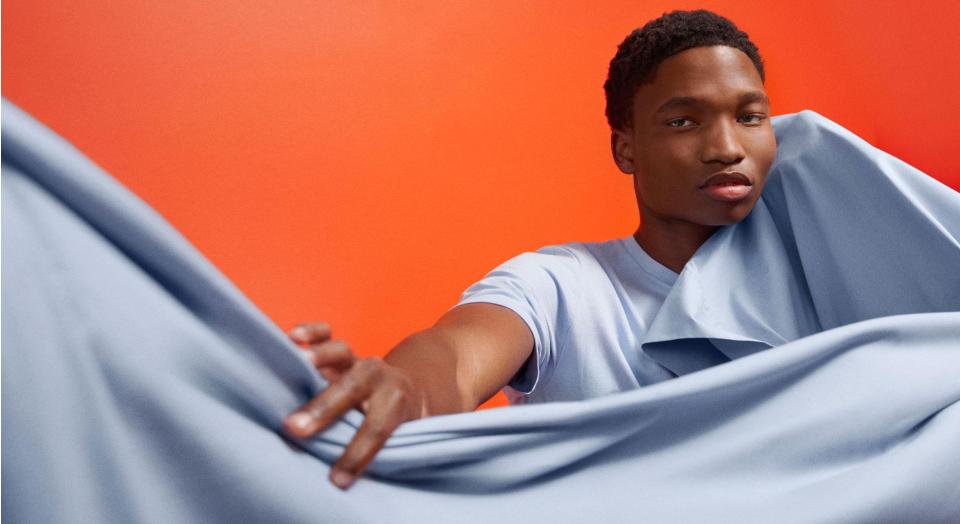 A young man wrapped in a light blue sheet and standing in front of a bright red wall