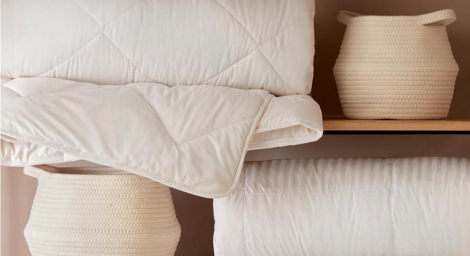 what do you need for a comfortable bed. close up shot of woven baskets and quilts stacked on wooden shelving.