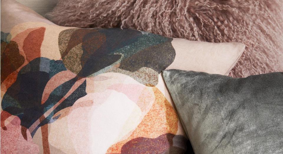 close up of styling cushions. layered floral cushion, textured shag cushion and velvet cushion stack.