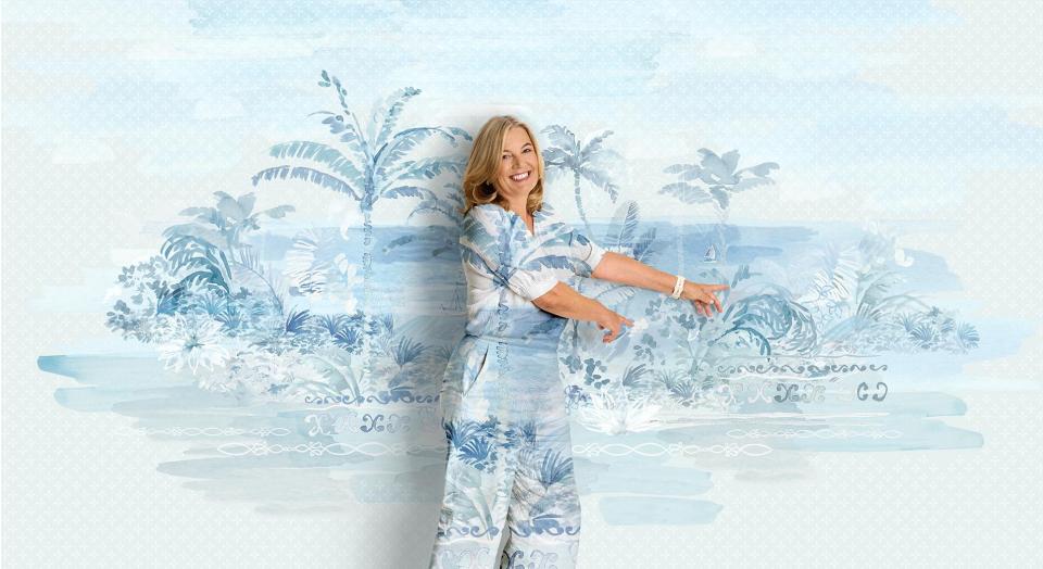 A woman stands, smiling in front of a painterly background. His shirt and pants are in the same matching artwork.