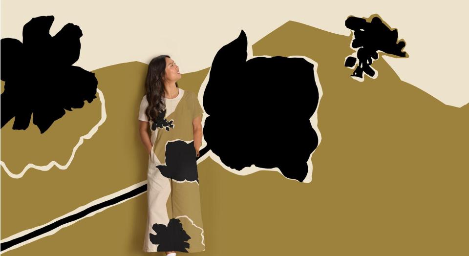 A woman stands, smiling in front of an abstract floral print background. Her jumpsuit is in the same matching pattern.