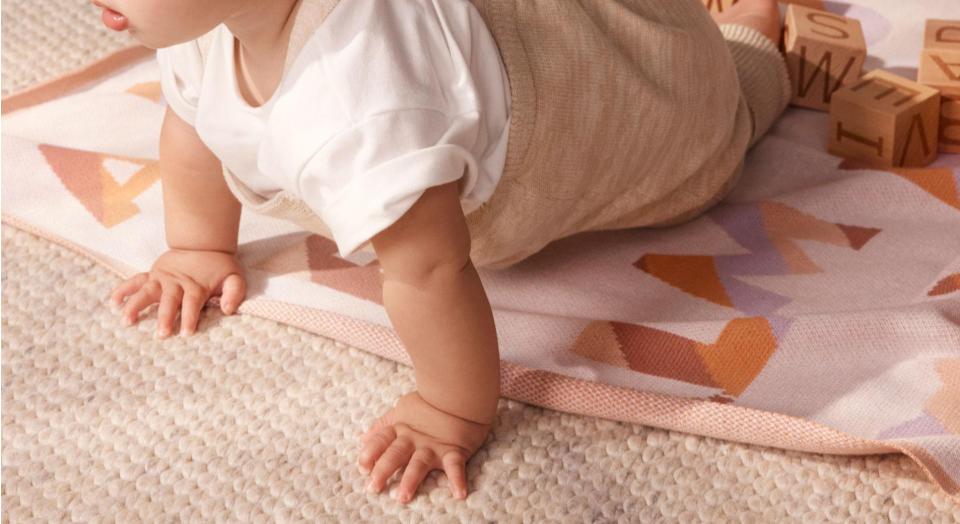 cropped landscape shot of baby enjoying tummy time on jute rug, with sheridan aleph blanket beneath him. he has his mouth open and looks alert, wearing a white tee with rolled up sleeves and beige joggers.