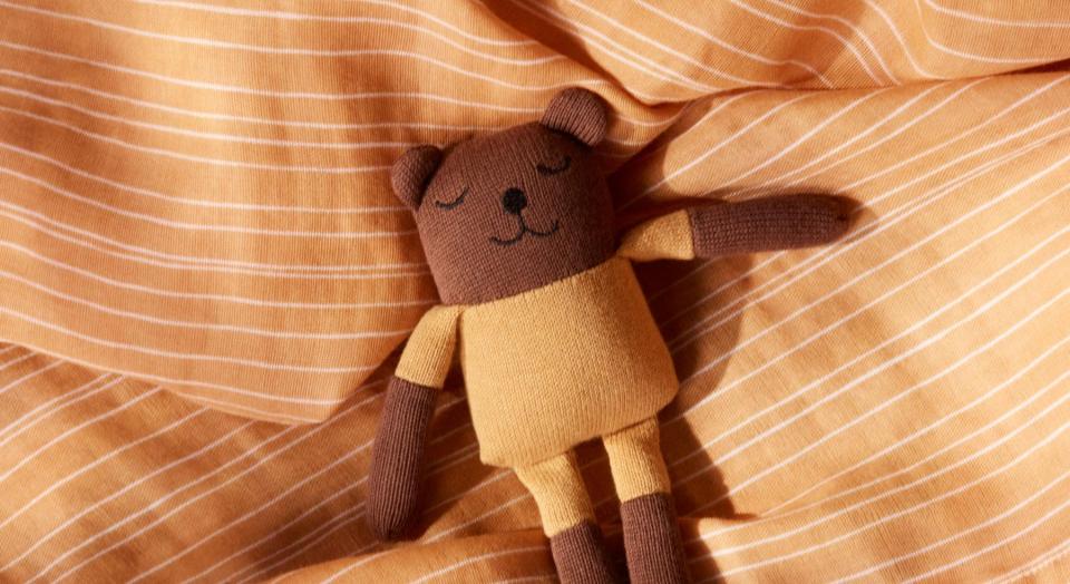 little brown bear toy crafted from leftover cotton yarn in orange shirt lies on orange cotton muslin baby wraps