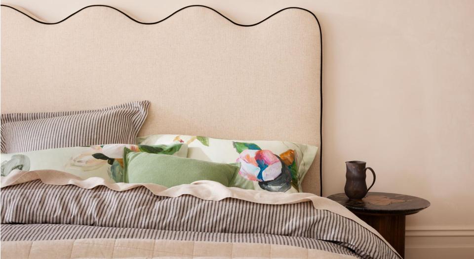 What is soft utility. Neutral coloured bed with grey striped sheets, scalloped fabric bed head and green floral cushions and pillows.