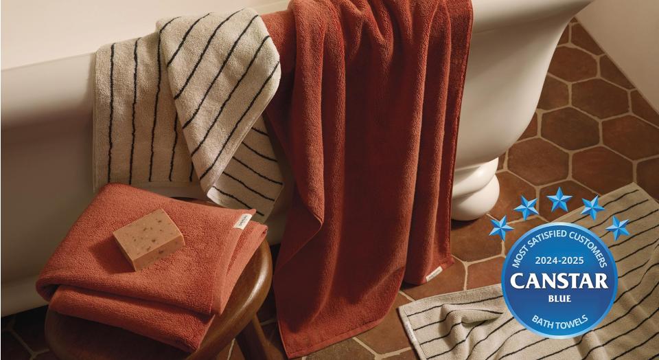 Aven bath towels in relish and limestone stripe draped over the side of a bath tub