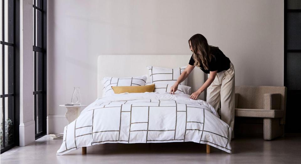 A woman making a bed with a geometric print quilt cover.