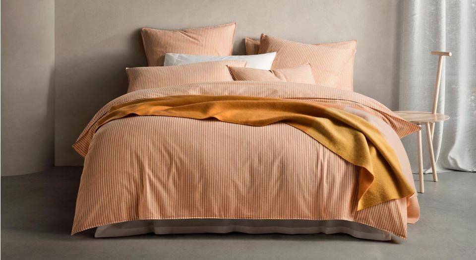 styled landscape shot of modern orange bedding, sheridan's reilly stripe marmalade bedding. layered with a wool blanket in a similar colour palettem and white pillow.