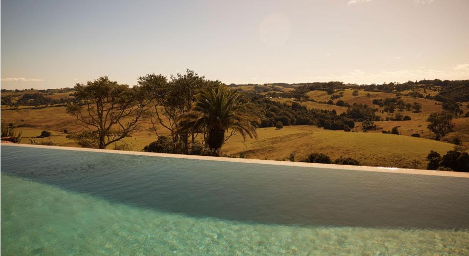 The edge of an outdoor swimming pool. In the background is a view of grassy hills and trees.