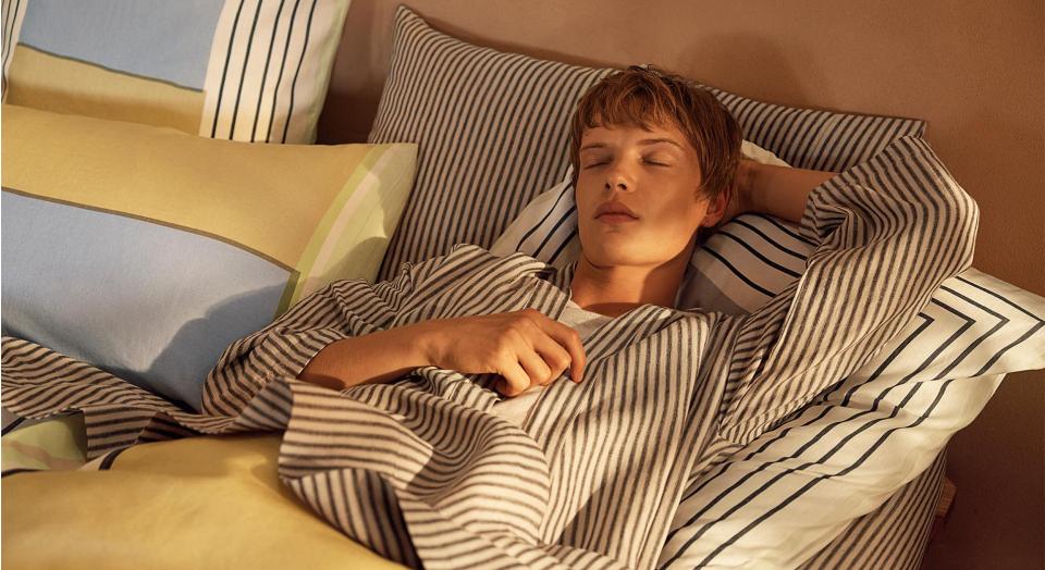 A young person rests in a bed, featuring contrast striped and geometric sheets