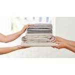 A pile of folded sheets and towels being passed from one set of hands to another