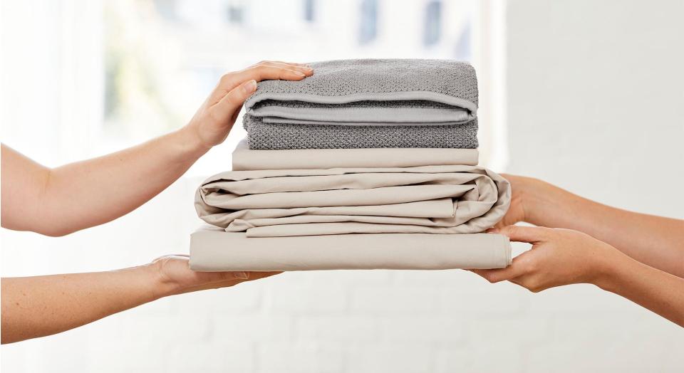 A pile of folded sheets and towels being passed from one set of hands to another
