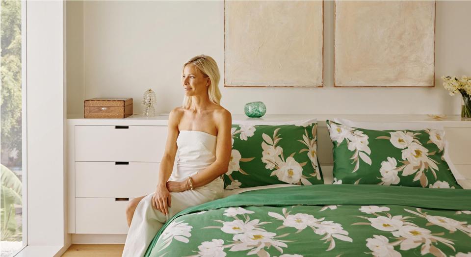 pip spiro, white woman with blonde hair wearing strapless white dress, sits on made up green bed, looking at the window of her home.