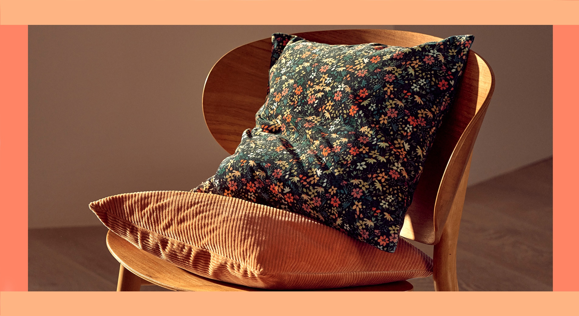 modern 70s style interior design, orange corduroy cushion and velvet floral cushion sit on wooden chair with curved back.