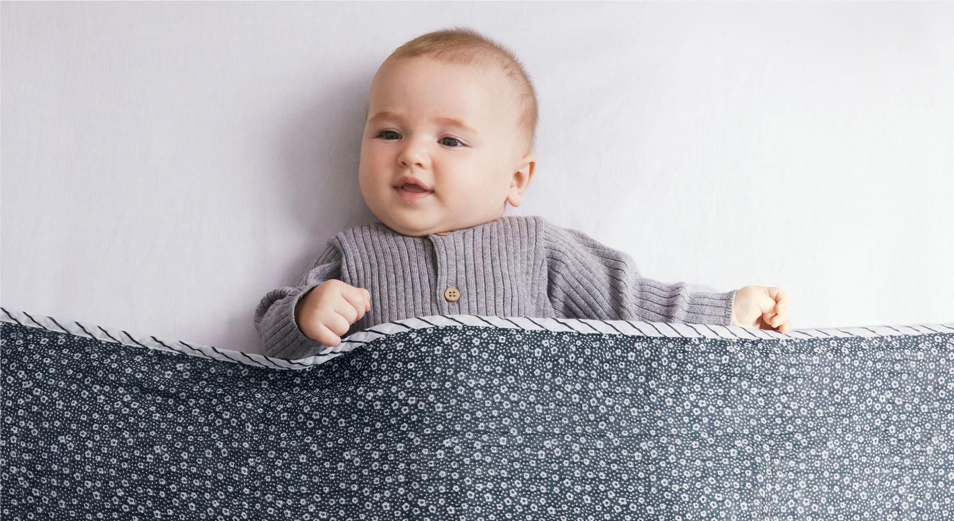 baby lying against silver sheet tucked into patterned bedding