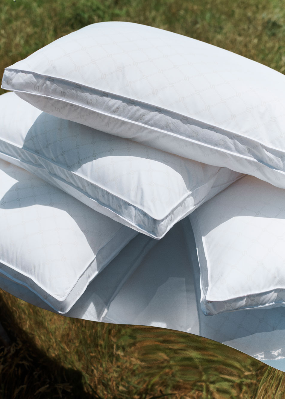 Photo of three pillows stack on top of one another. They're sitting on top of a mirrored podium in a grass field.