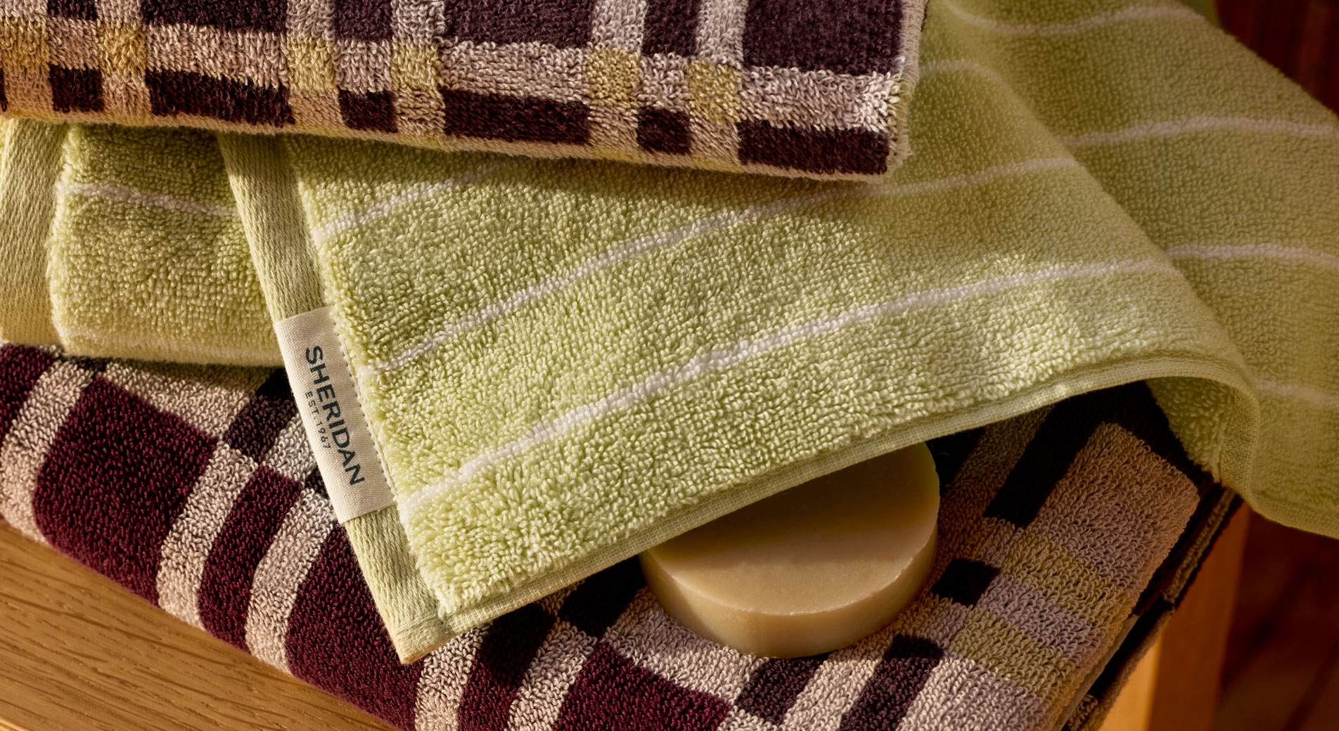 A pile of folded Sheridan bath towels. A round block of soap sits between two of the layers.
