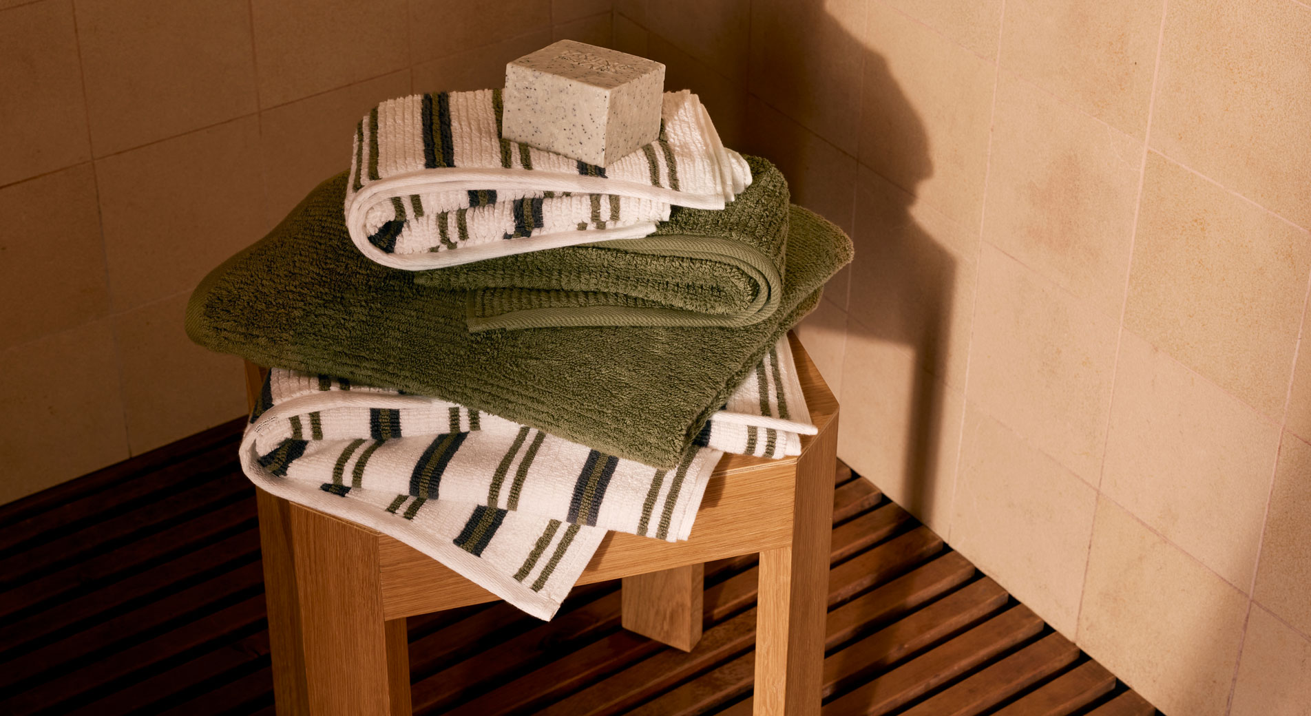 A stack of folded Living Textures towels in the colour jungle and jungle stripe. A block of soap sits on top of the towels.