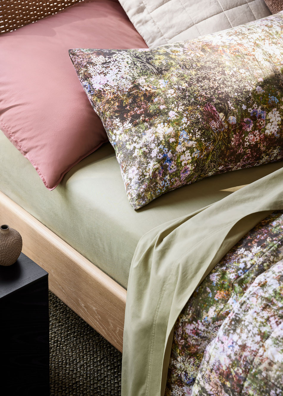 A close-up of a bed with green sheets and a floral linen bed cover