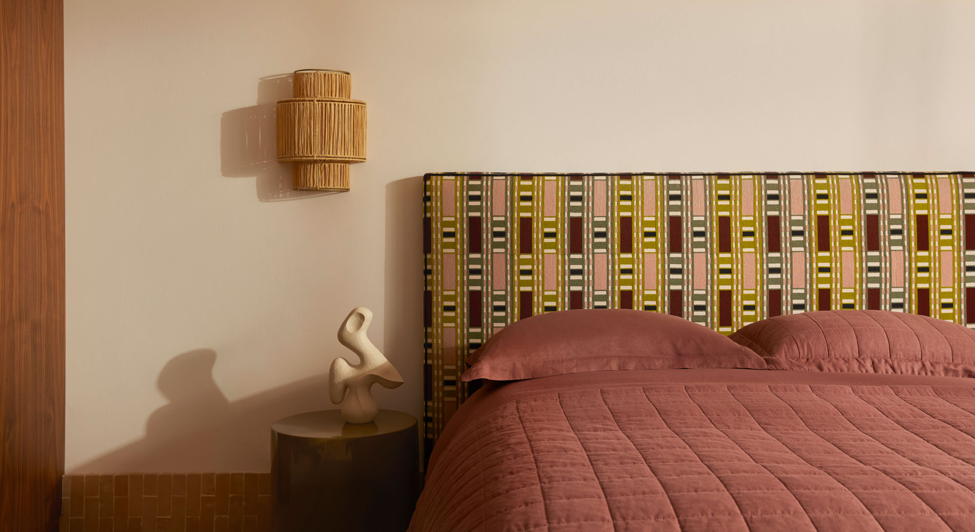 A bed with a geometric patterned bed head, made up simply with a bed cover and two pillows