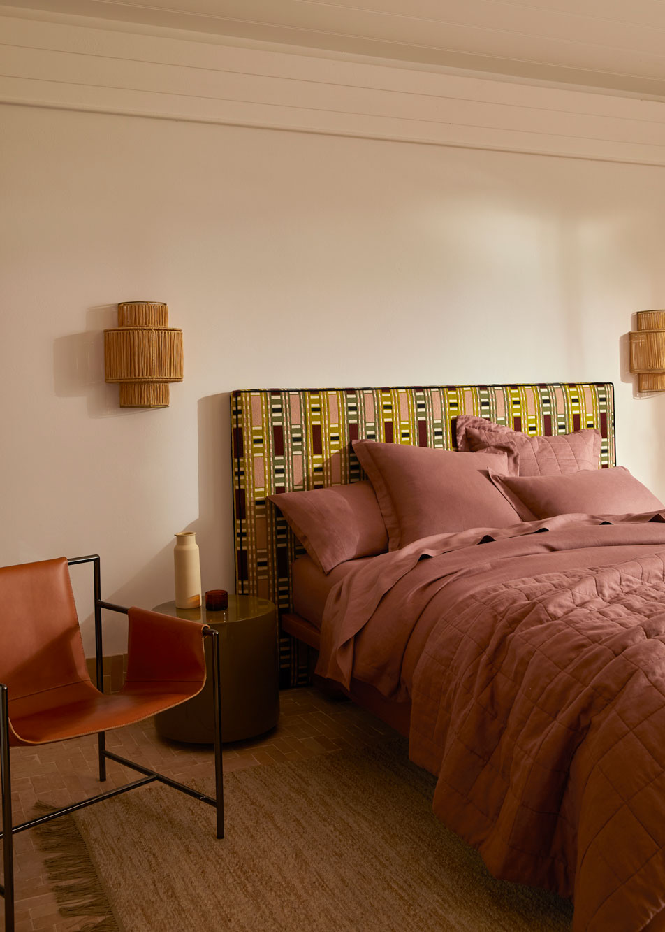 A bed with a geometric patterned bed head. Next to the bed is a leather armchair and a table