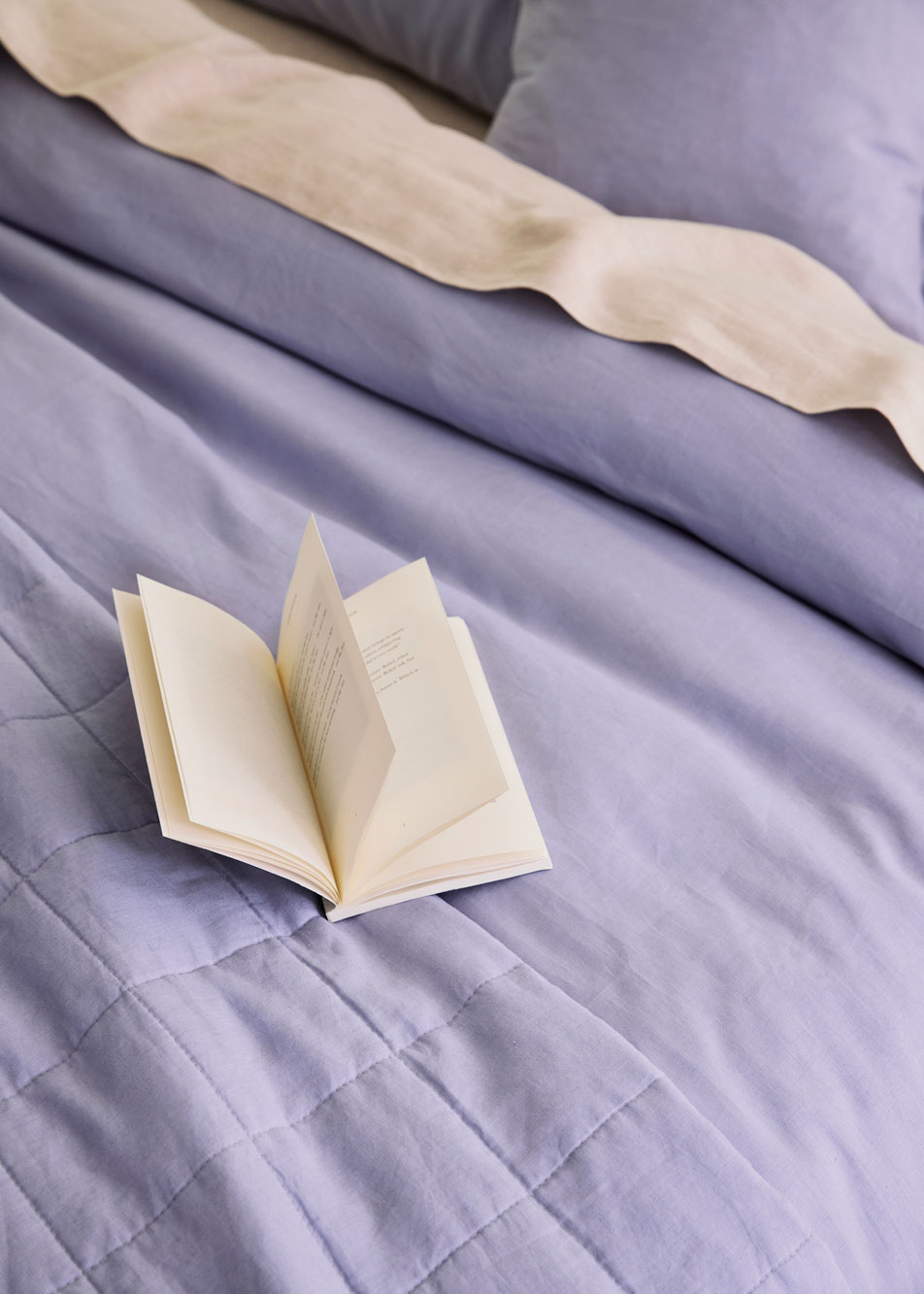 An open book sitting on top of a bed, made with purple bed linen