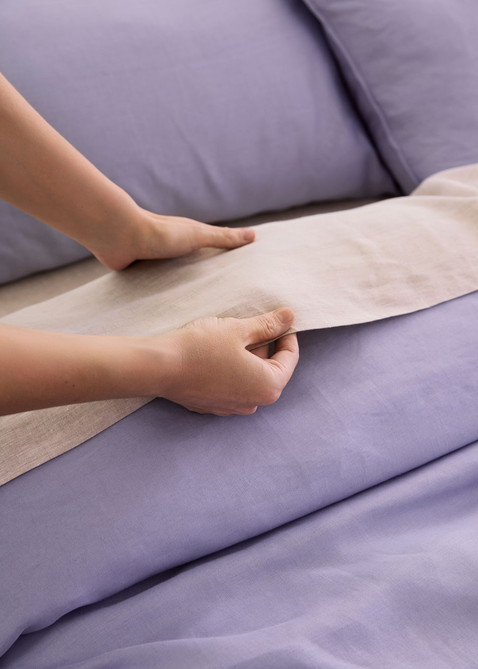 A pair of hands straightening a linen bed sheet