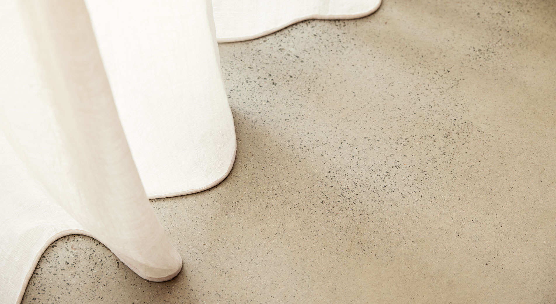 A white linen curtain hanging above a concrete floor