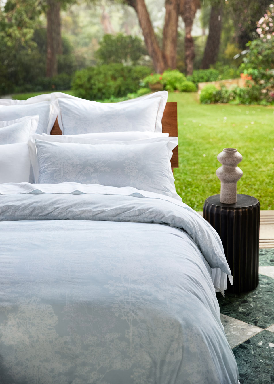 A light blue bed in an open room, with a lush green garden behind it.
