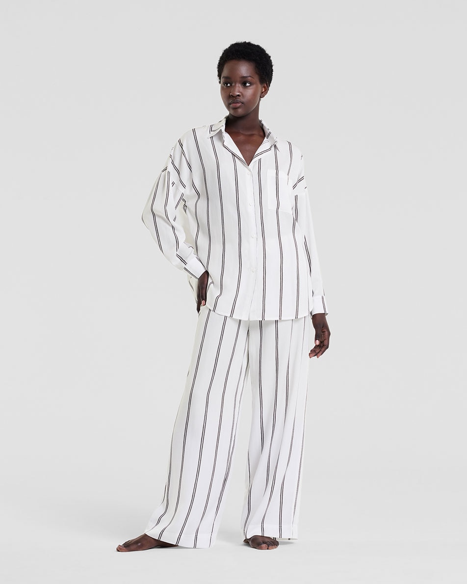 A young woman in front of a white backdrop, modelling the Audra loungewear shirt and pants