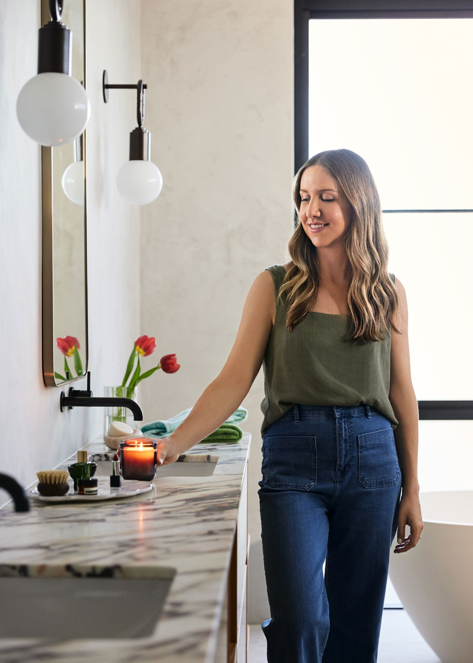A young woman placing a lit candle on a marble bathroom vanity.