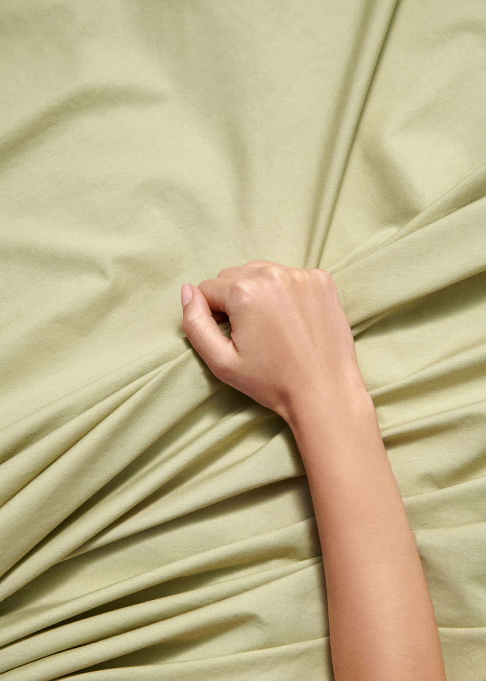 A hand holding onto a pale green sheet
