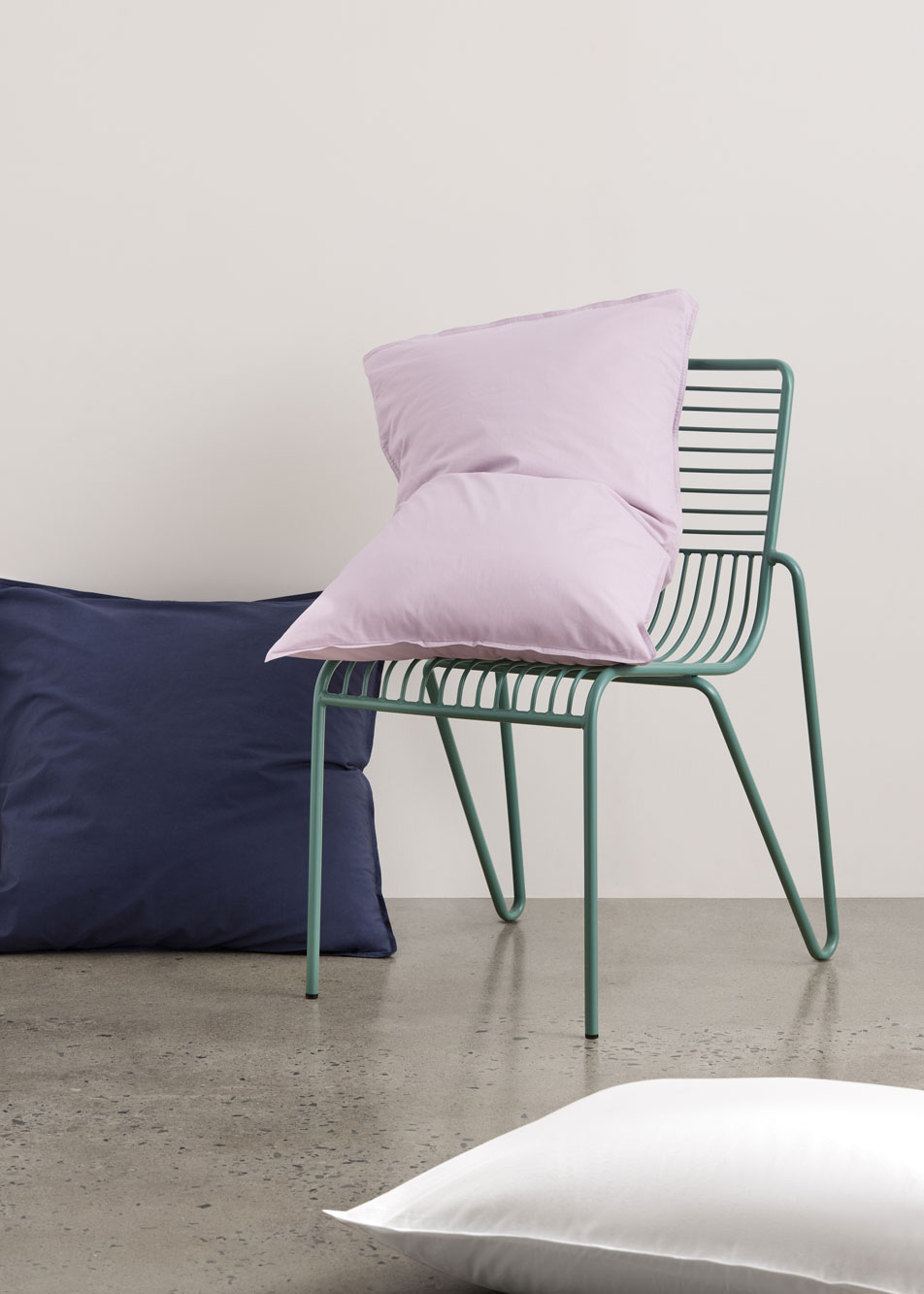 Three pillows in different colours. One is propped up on a chair and two are laying on the floor beside.