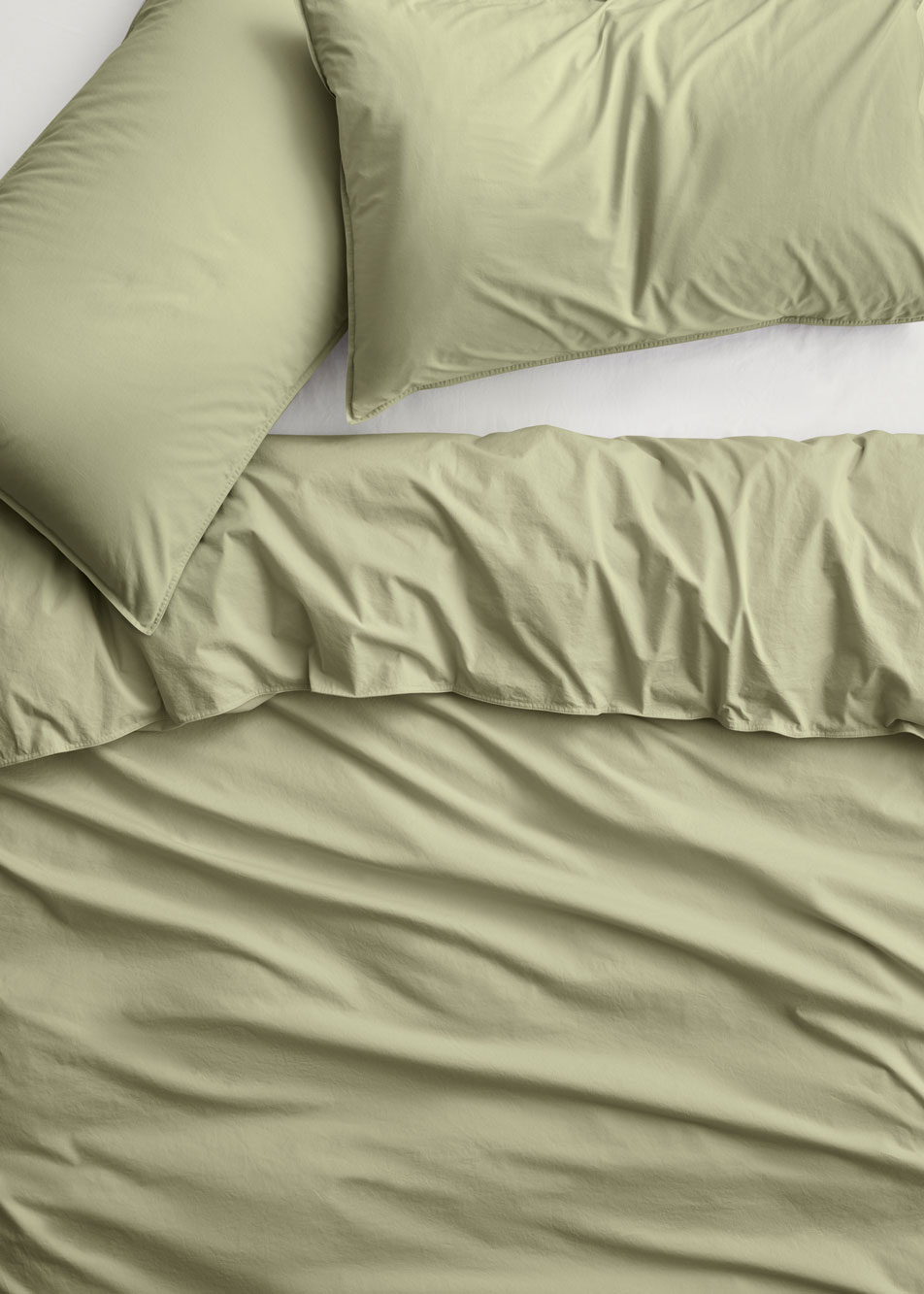 A close up of a bed dressed in Bayley Washed Percale bedding in the colour soft fern