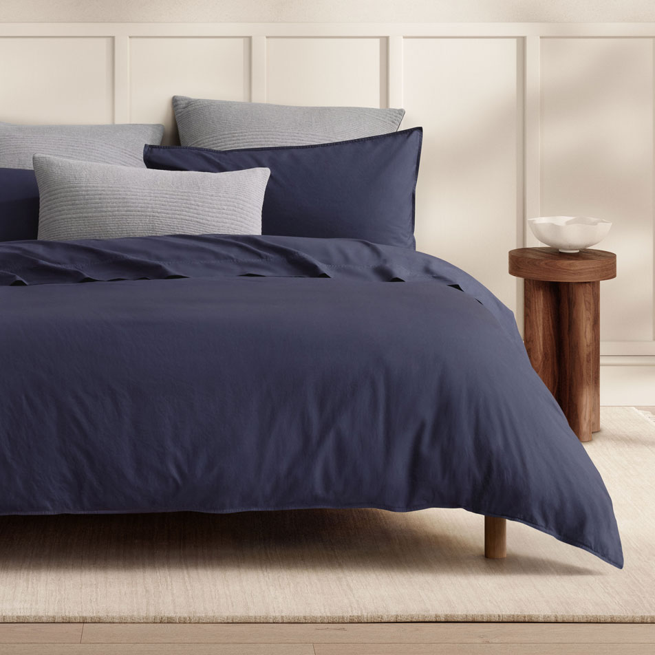 A bed dressed in Bayley Washed Percale bedding in the colour deep sea