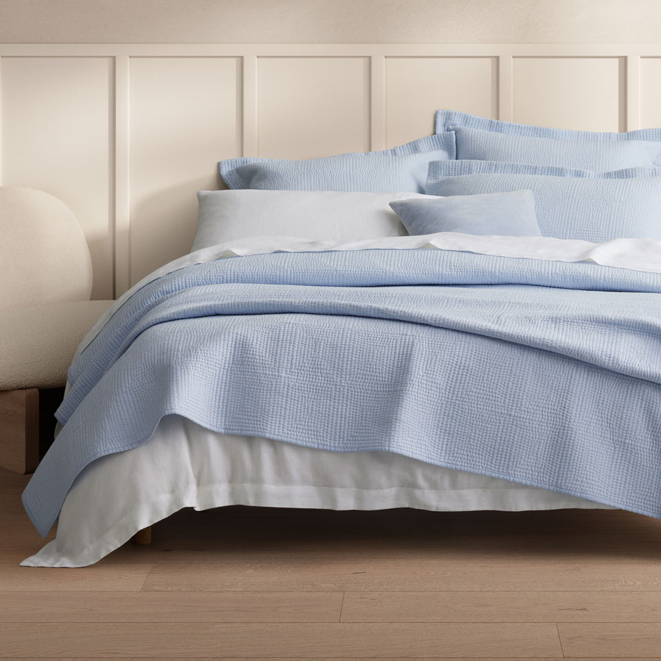 A bed with blue and white bedding, with a bed cover draped over the end.