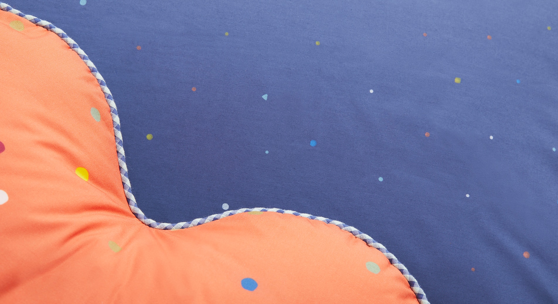 Kids sleep transition. A close up photo of an orange heart-shaped cushion on top of a blue sheet with small hearts printed on it.