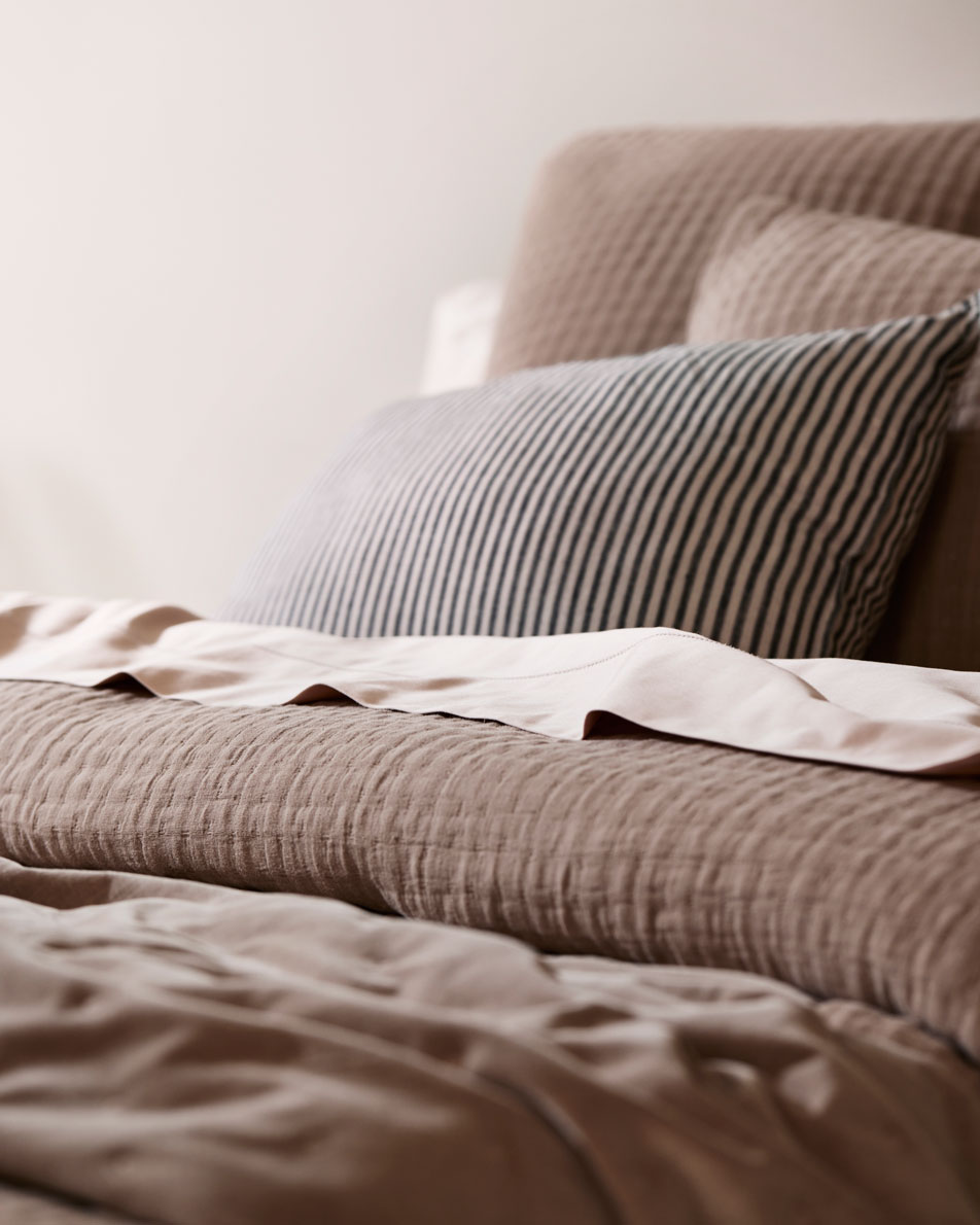 A close-up of a bed made with rose pink sheets, mocha brown bedding and a black and white striped accent cushion