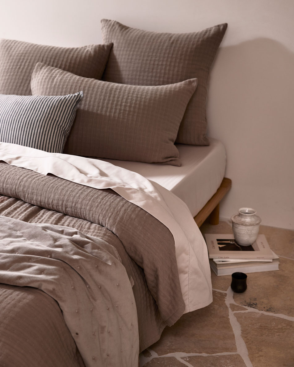 A close-up of a bed made with rose pink sheets, mocha brown bedding and a black and white striped accent cushion