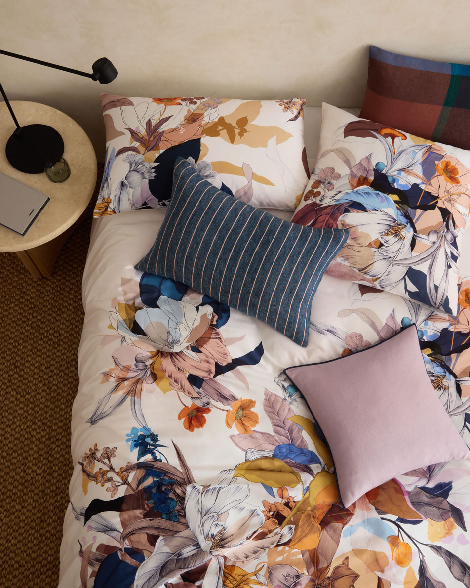 An overhead shot of a floral bed with three different patterned cushions on it