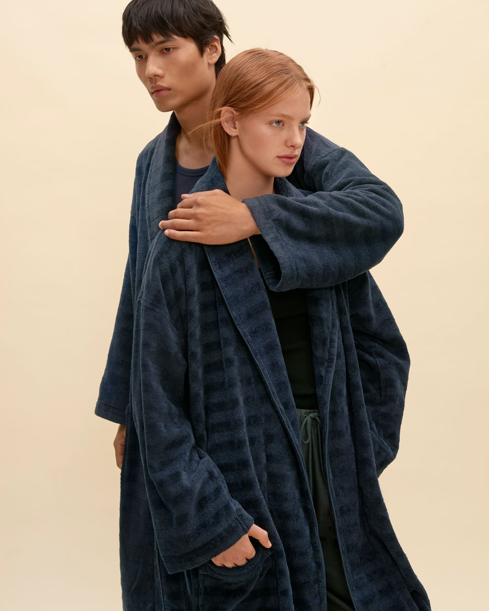 Two models leaning on each other, both wearing navy Sheridan bathrobes.