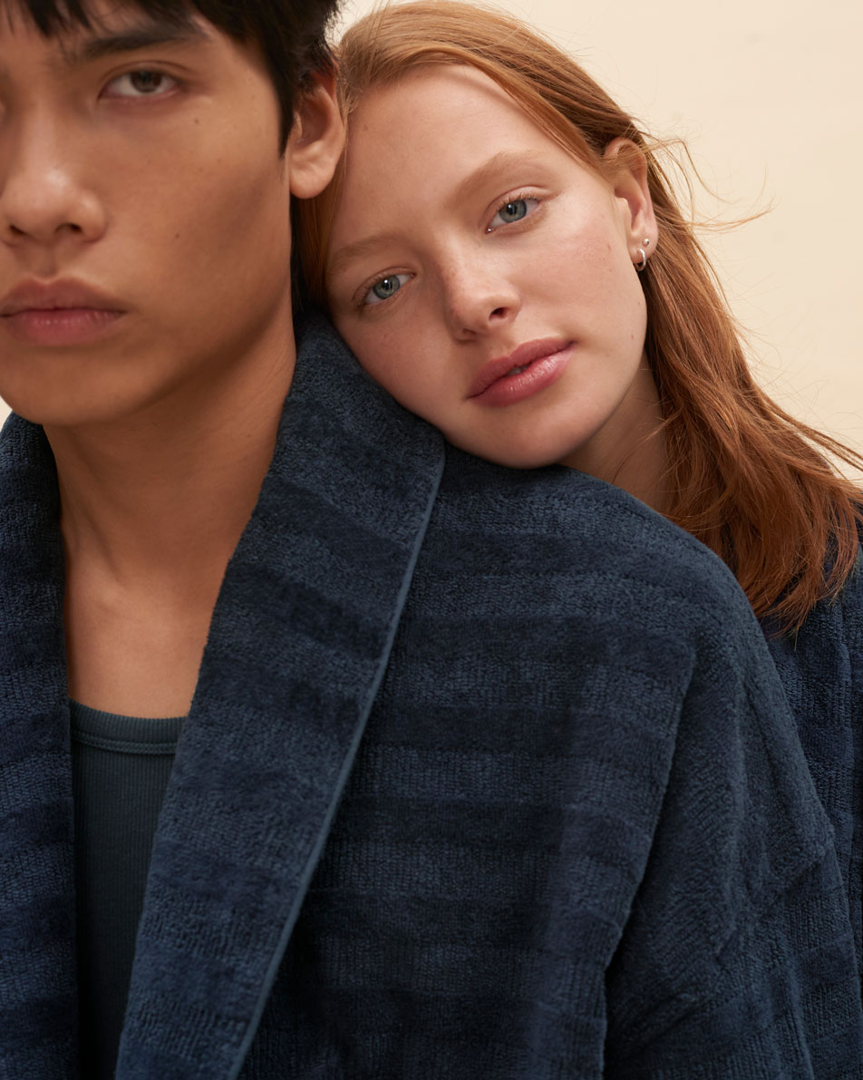 Two models leaning on each other, both wearing navy Sheridan bathrobes.