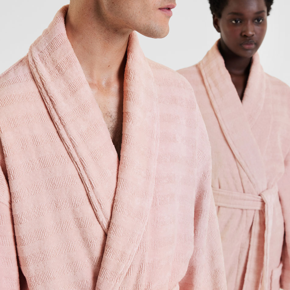 A close up image of two models wearing light pink bathrobes in front of a white background