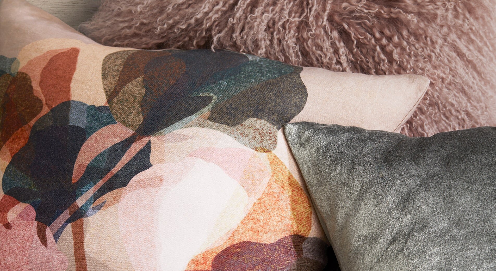 close up of styling cushions. layered floral cushion, textured shag cushion and velvet cushion stack.