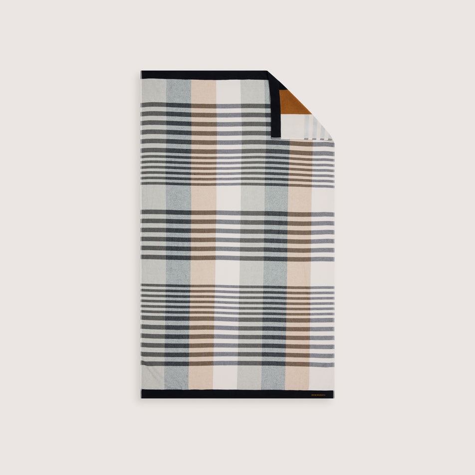 A flat lay image of a beach towel with a geometric design in shades of black, white and brown