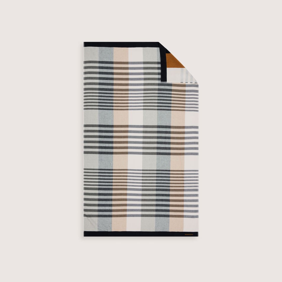 A flat lay image of a beach towel with a geometric design in shades of black, white and brown