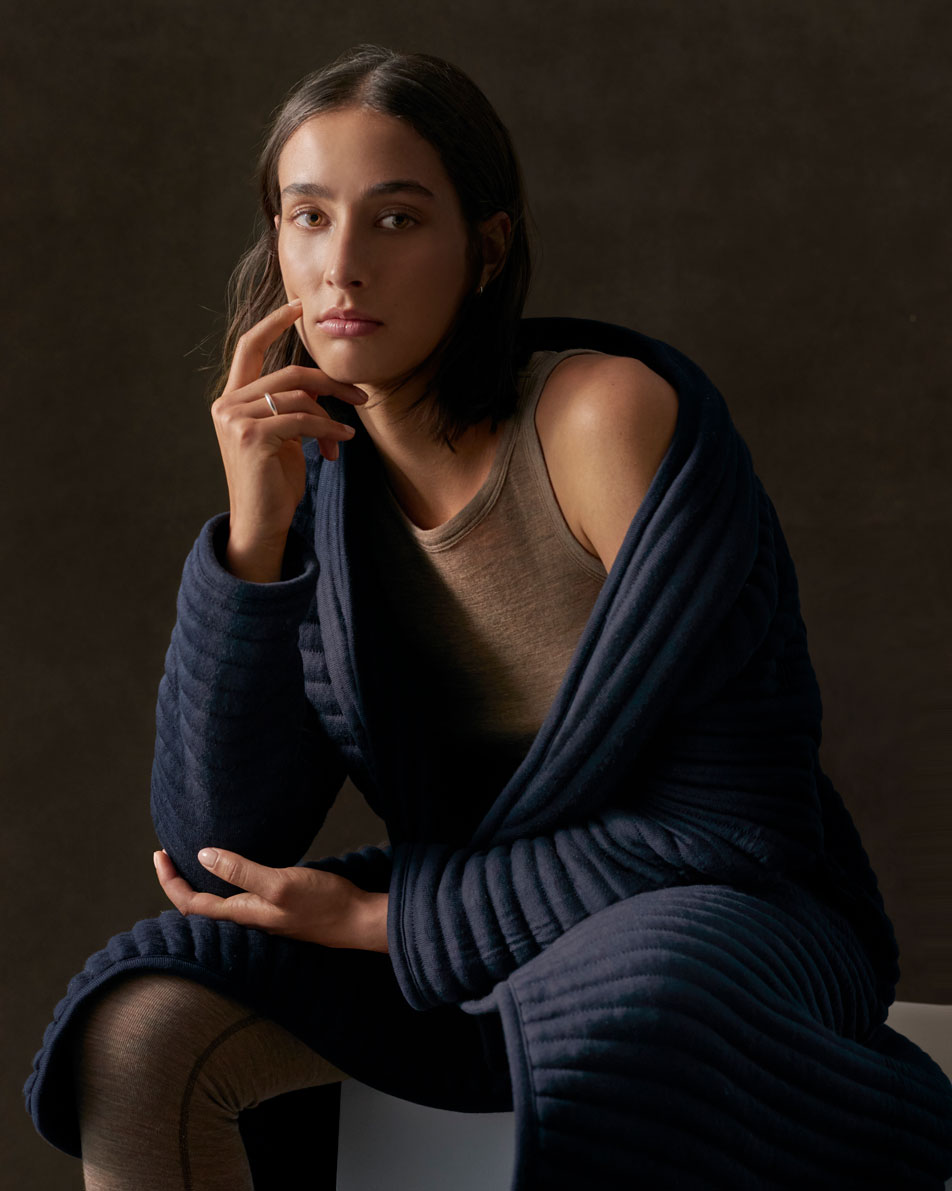 An image of a young woman with short brown hair, wearing a navy Sheridan bathrobe.