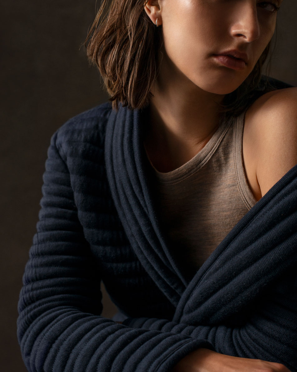 A cropped image of a young woman with short brown hair, wearing a navy Sheridan bathrobe.