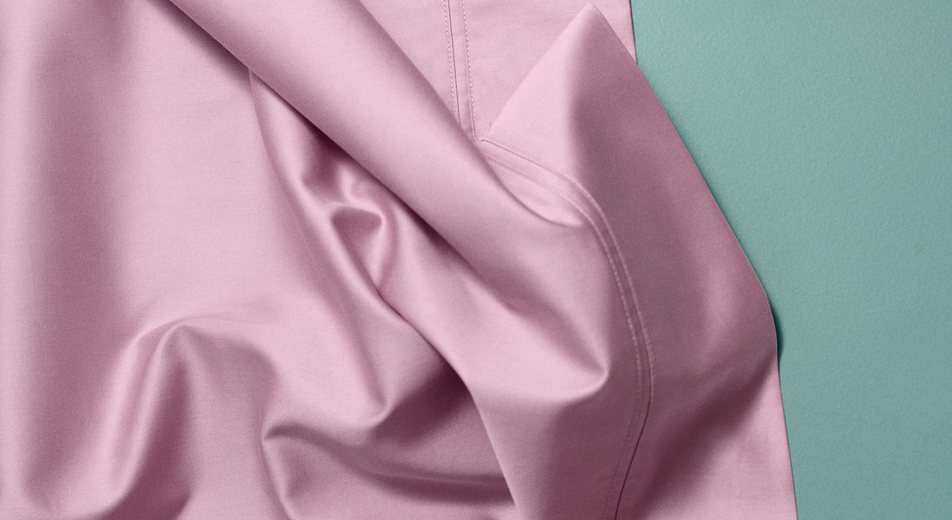 A close-up of a pale pink sateen sheet lying tousled on a teal backdrop